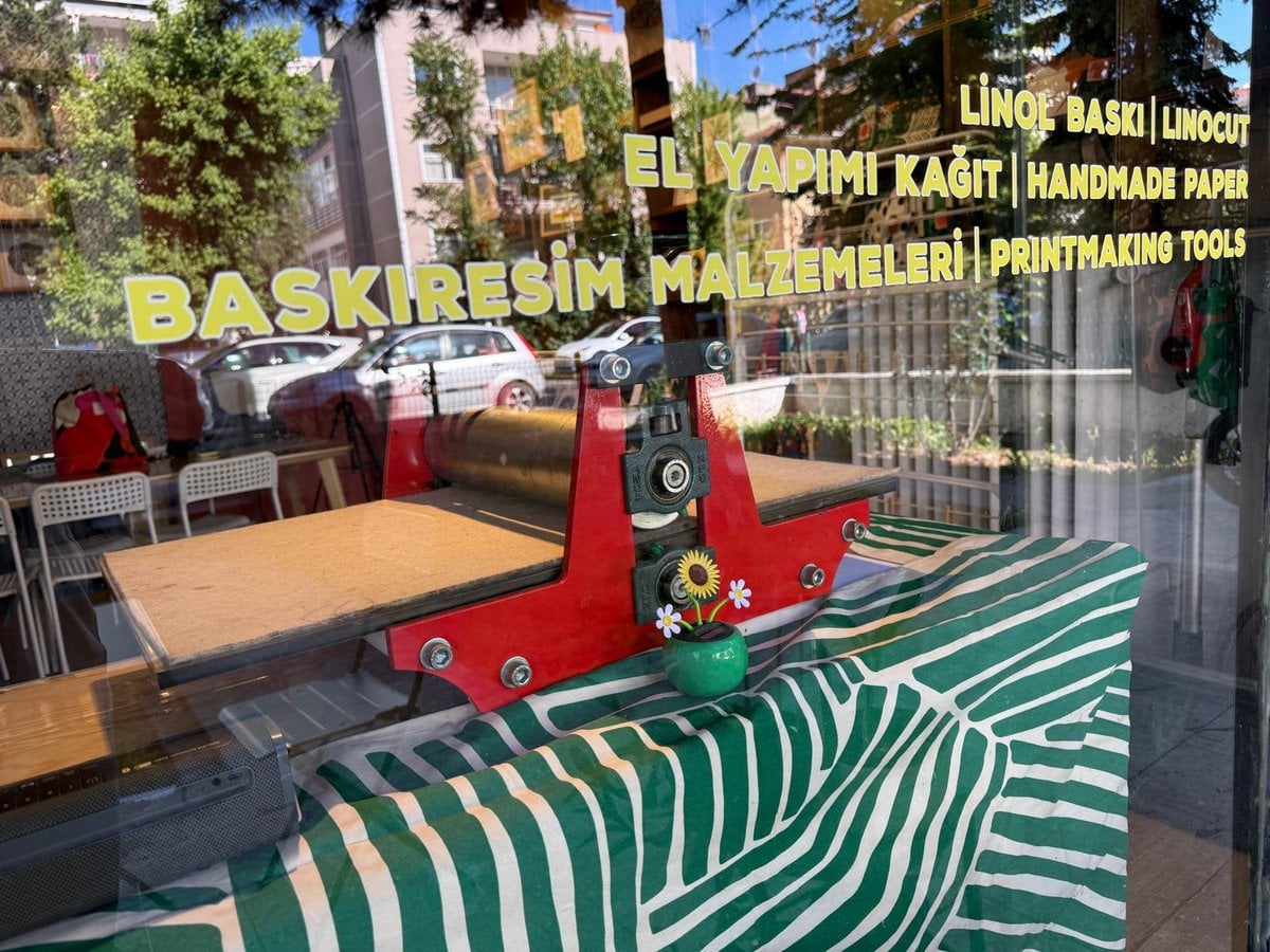 Kırmızı baskı presi — yeşil çizgili tezgahta, ardında vitrin ışığı